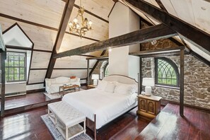 A spacious attic bedroom with a large bed, a bench, and a sofa. There are stone walls and wooden beams. - Stunning Historic Maine Stone Castle (Bath)