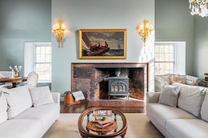 A living room with a fireplace, two sofas, a coffee table, and a painting above the fireplace. - Stunning Historic Maine Stone Castle (Bath)