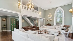 A spacious living room with a high ceiling, a staircase, and a large window. - Stunning Historic Maine Stone Castle (Bath)