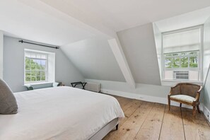 A bedroom with a sloped ceiling, a bed, a chair, and two windows. - Stunning Historic Maine Stone Castle (Bath)