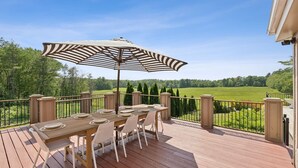 A wooden deck with a table and chairs, an umbrella, and a view of a green field. - Stunning Historic Maine Stone Castle (Bath)