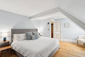 A bedroom with a large bed, a chair, and a door leading to another room. - Stunning Historic Maine Stone Castle (Bath)