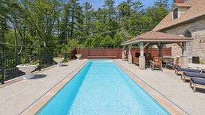 A rectangular swimming pool with a stone deck, surrounded by a wooden fence and a gazebo with seating. - Stunning Historic Maine Stone Castle (Bath)