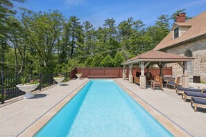 A rectangular swimming pool with a stone deck, surrounded by a wooden fence and a gazebo with seating. - Stunning Historic Maine Stone Castle (Bath)