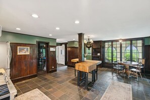 A spacious room with a large dining table, a kitchen area, and a view of the outdoors through large windows. - Stunning Historic Maine Stone Castle (Bath)