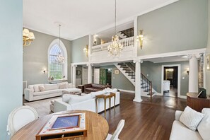 A spacious living area with a high ceiling, a grand staircase, and a chandelier. - Stunning Historic Maine Stone Castle (Bath)