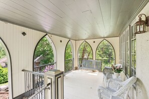 A covered porch with a bench and wicker chairs, featuring arched windows and a railing. - Stunning Historic Maine Stone Castle (Bath)
