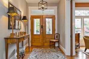 Une porte en bois avec un panneau de verre, une console surmontée de lampes, une chaise et un tapis à motifs.