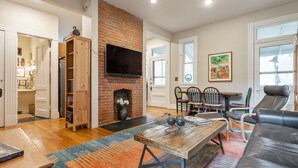 Una sala de estar con chimenea de ladrillo, un televisor montado encima y una zona de comedor con sillas y una mesa.