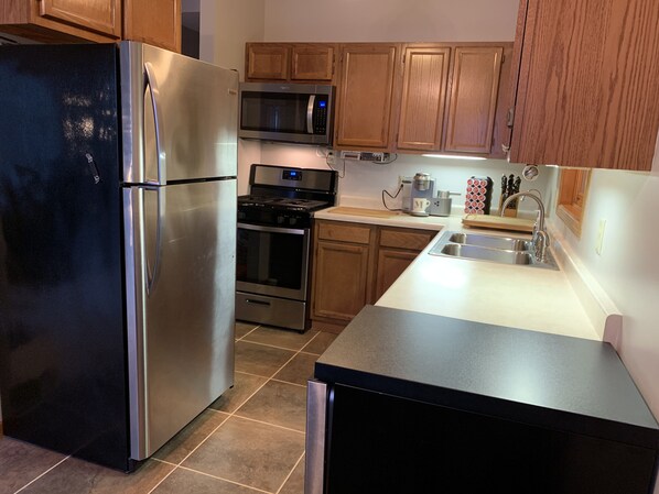 Uma cozinha moderna com eletrodomésticos de aço inoxidável, armários de madeira e bancada preta.