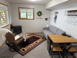 A cozy room with a sofa, a wooden table, a wheelchair, a fireplace, and a window with blinds.