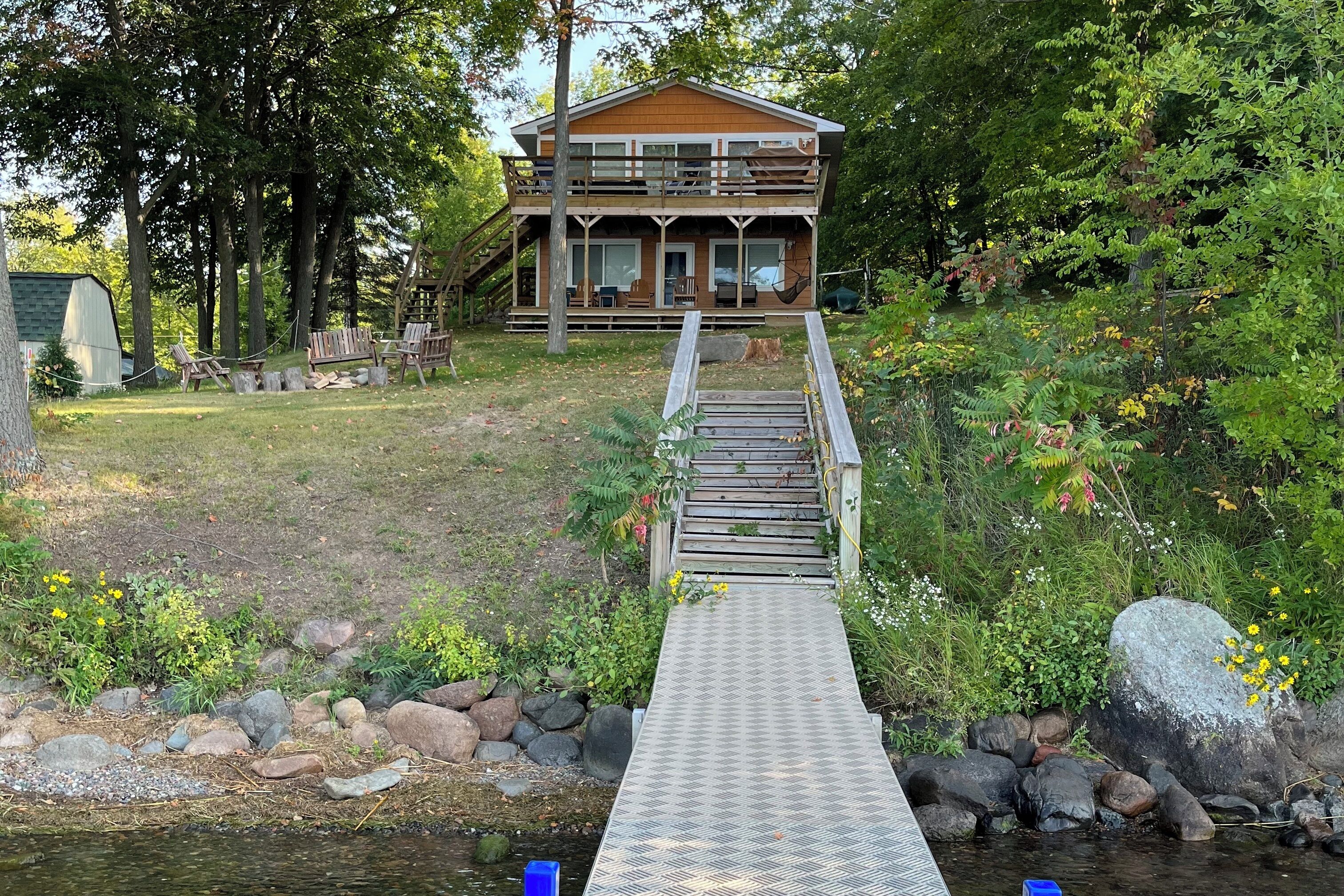 A wooden deck leading to a two-story cabin with a porch and outdoor seating.