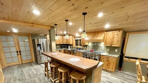 Una cucina moderna con mobili in legno, un'isola centrale con sgabelli, elettrodomestici in acciaio inossidabile e luci a sospensione.