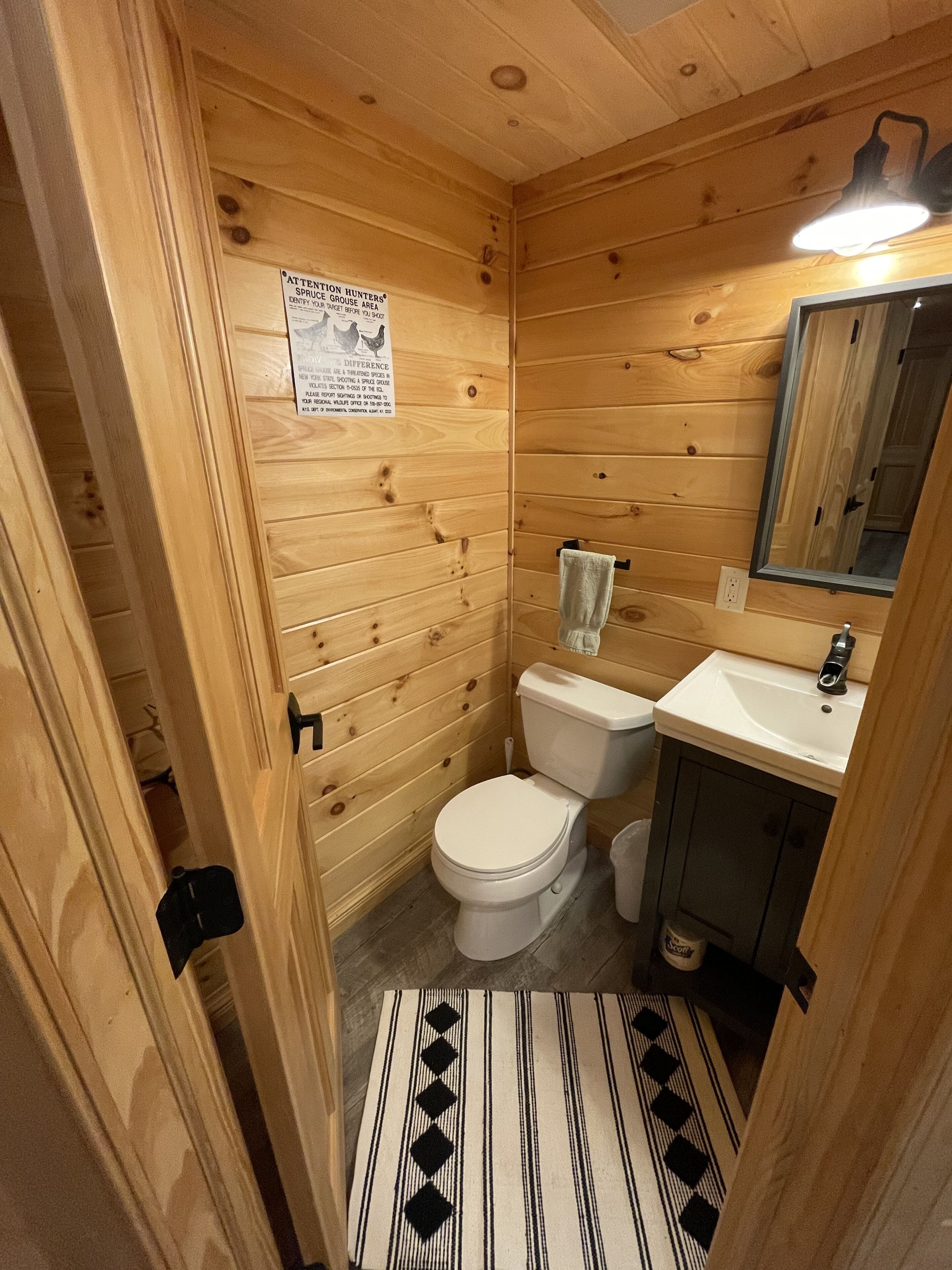 A wooden-paneled bathroom with a toilet, sink, and mirror.