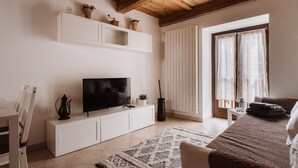A modern living room with a flat-screen TV on a white cabinet, a wooden ceiling, and a large window with curtains. - Mezzanine apartment in an alpine hamlet (Roure)