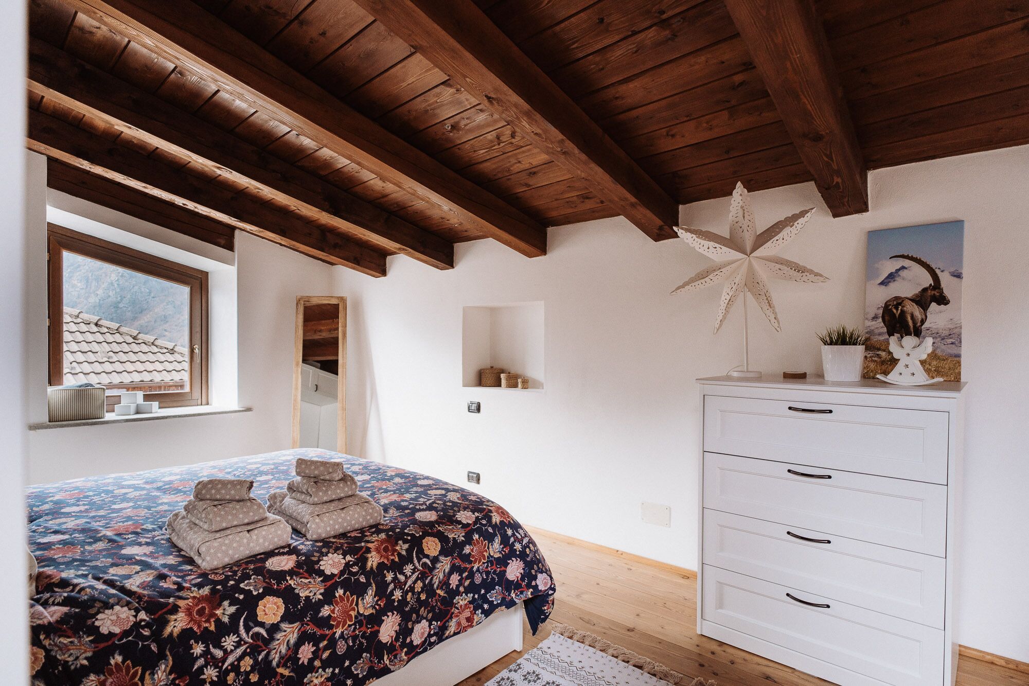 A bedroom with a wooden ceiling, a bed with a floral bedspread, a dresser, and a star decoration on the wall.
