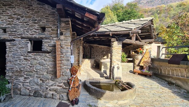 A rustic stone building with a wooden staircase leading to a door, a small window, and a stone well in the courtyard. - Mezzanine apartment in an alpine hamlet (Roure)