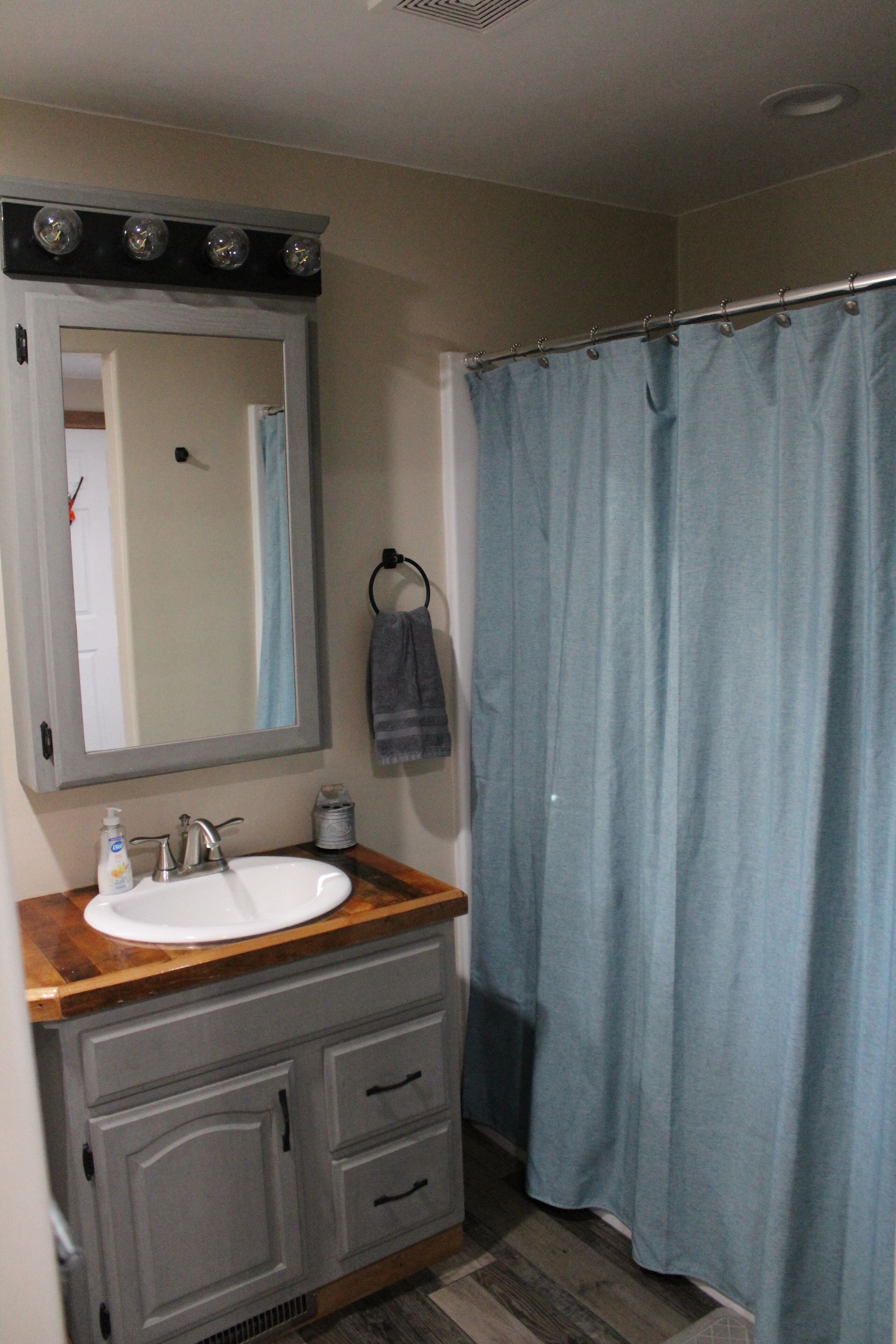 Une salle de bain avec un lavabo blanc, un miroir avec éclairage intégré, un porte-serviettes et un rideau de douche bleu.