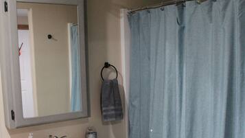 Une salle de bain avec un lavabo blanc, un miroir avec éclairage intégré, un porte-serviettes et un rideau de douche bleu.