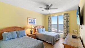 Une chambre d’hôtel avec deux lits, un ventilateur de plafond, une télévision, un bureau et une vue sur la mer.