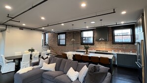 A modern kitchen with a central island, a grey sectional sofa, and a staircase leading to an upper level. - Premier penthouse  w Private Rooftop near Memorial Stadium & Pinnacle Arena!   (Lincoln)