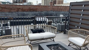 A rooftop patio with wicker furniture, a square black table, and a metal railing. - Premier penthouse  w Private Rooftop near Memorial Stadium & Pinnacle Arena!   (Lincoln)