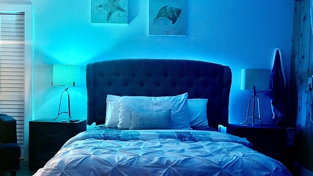 Ein Schlafzimmer mit einem großen Bett, einem Kopfteil, einem Nachttisch, einer Lampe und Wandbildern.