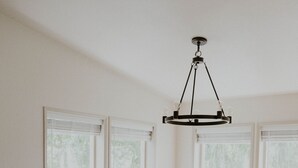 A dining area with a wooden table and six chairs, a chandelier, and large windows with blinds. - Cheerful Country Cottage (Rexburg)