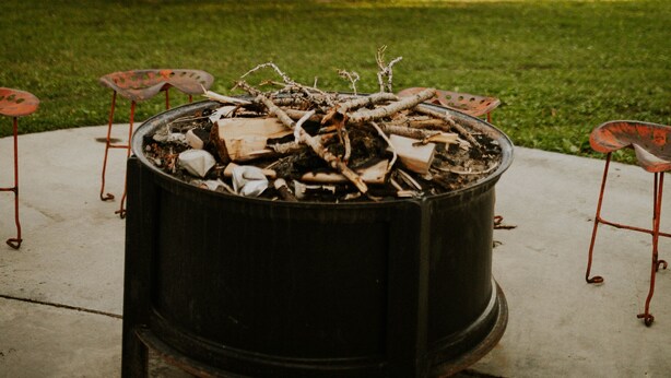 A fire pit with logs in the center, surrounded by metal chairs. - Cheerful Country Cottage (Rexburg)