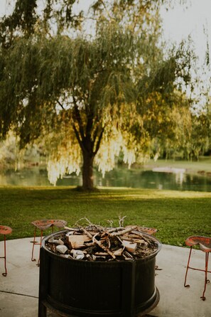 A fire pit with logs in the center, surrounded by metal chairs. - Cheerful Country Cottage (Rexburg)