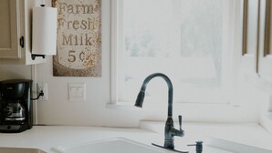 A kitchen with a white countertop, a sink, a coffee maker, and a wall-mounted sign reading "Farm Fresh Milk 5¢". - Cheerful Country Cottage (Rexburg)