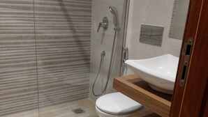 Moderni kylpyhuone, jossa on lasinen suihkuseinä, valkoinen wc-istuin ja pesuallas, jonka yläpuolella on puinen taso.