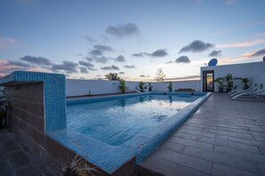Piscina no terraço com borda em azulejos, rodeada por plantas em vasos e espreguiçadeiras.