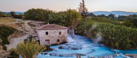 A stone building with a tiled roof near a cascading waterfall and terraced pools.