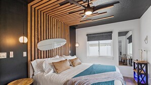 Ein modernes Schlafzimmer mit einem Bett, einer Wand aus Holzlatten, einem Deckenventilator und einem Fenster.