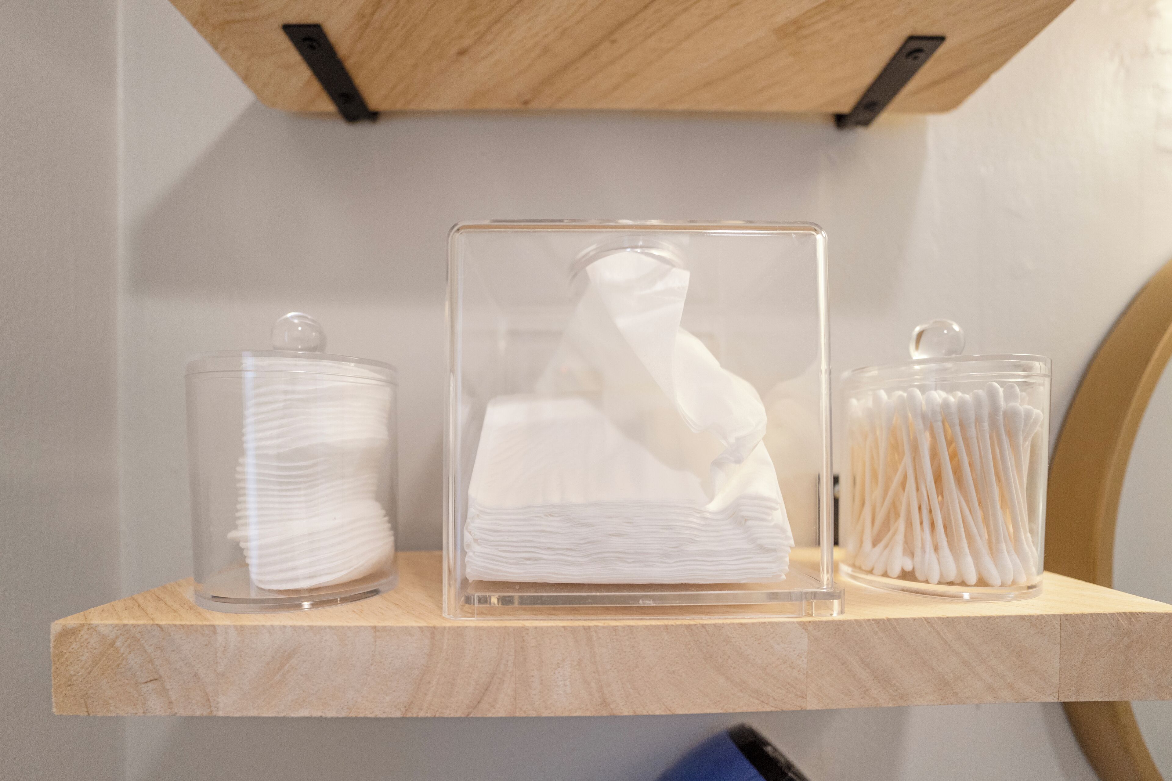 Three clear glass containers on a wooden shelf, each holding white cotton swabs.