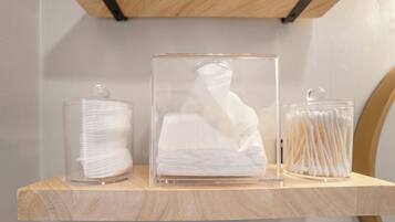 Three clear glass containers on a wooden shelf, each holding white cotton swabs.
