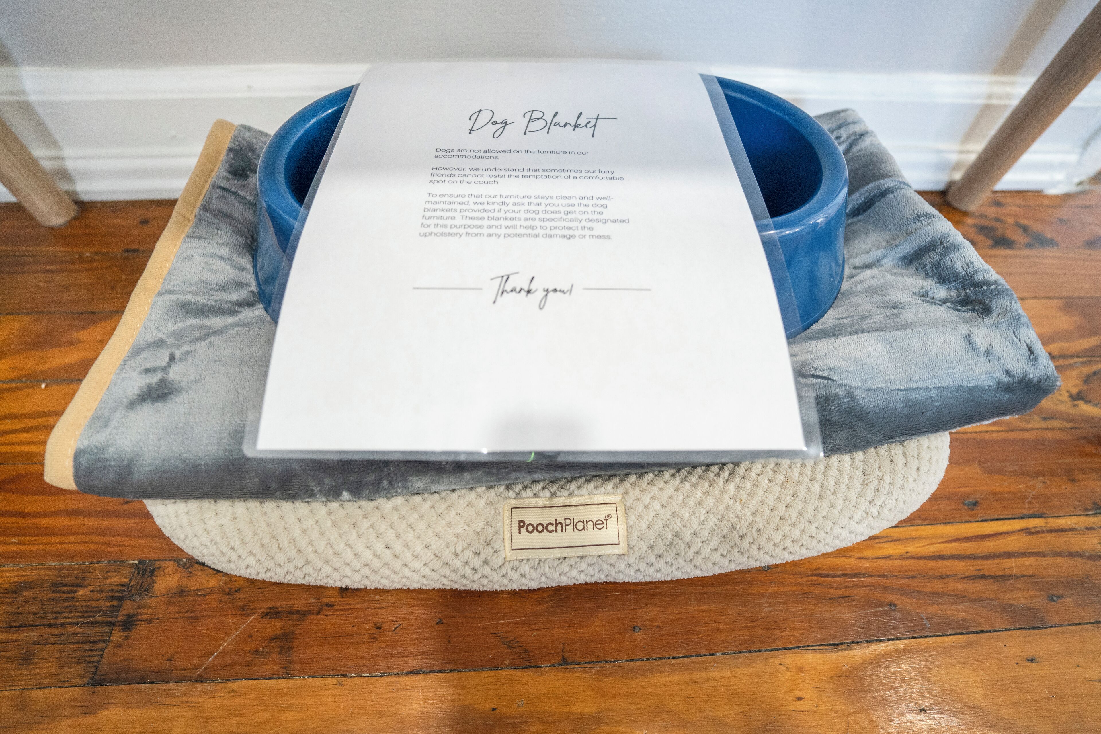 Uma cama para cachorro com etiqueta, uma tigela azul e um pedaço de papel com texto.