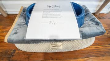 Uma cama para cachorro com etiqueta, uma tigela azul e um pedaço de papel com texto.