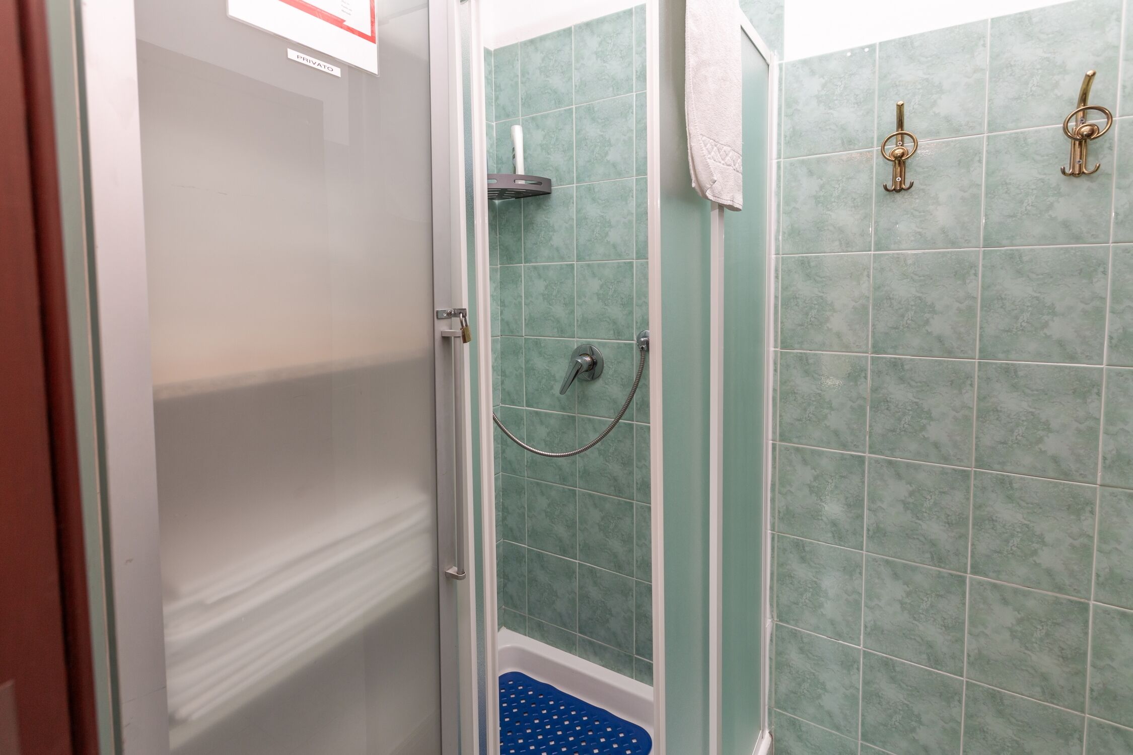A shower area with a glass door, a blue shower seat, and a towel hanging on a hook.