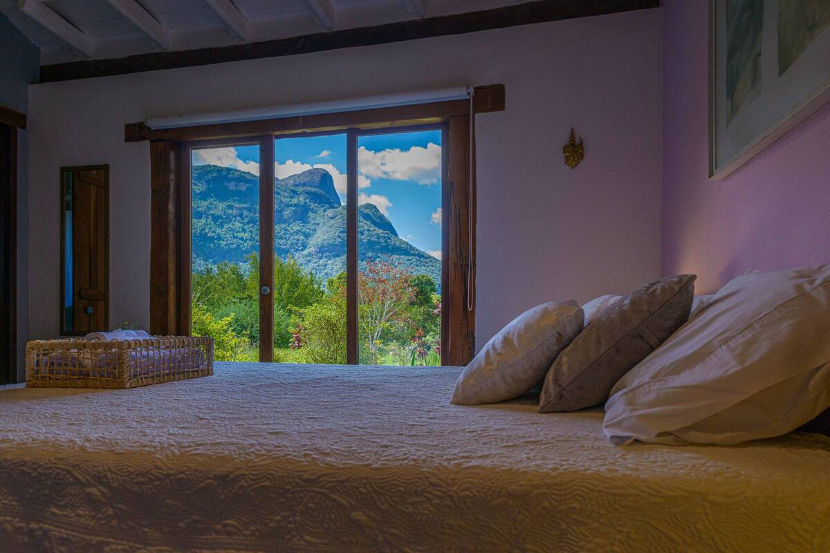 Un dormitorio con una cama grande, cabecera de madera y vistas a la montaña a través de una puerta corredera.