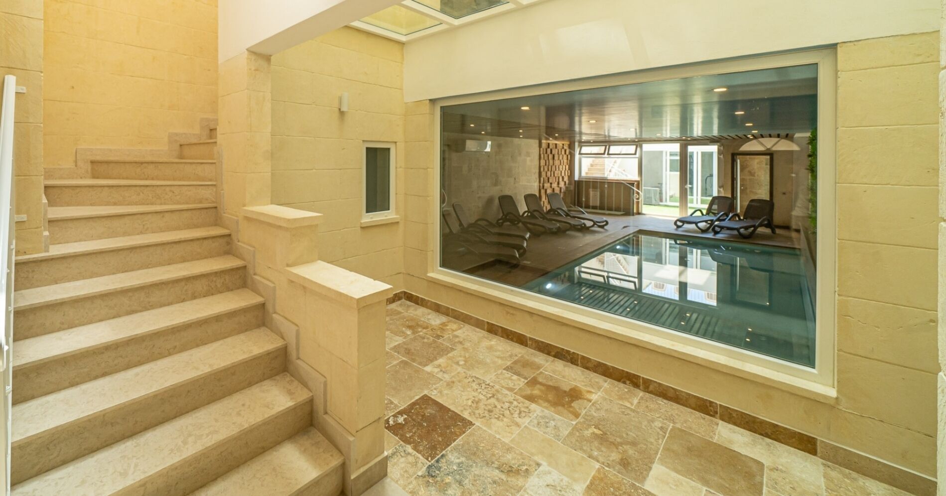A swimming pool with a glass wall, a staircase, and a view of the pool area.