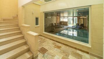 A swimming pool with a glass wall, a staircase, and a view of the pool area.