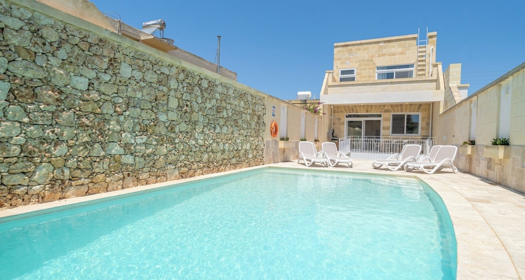 Piscina com parede de pedra e um edifício ao fundo.