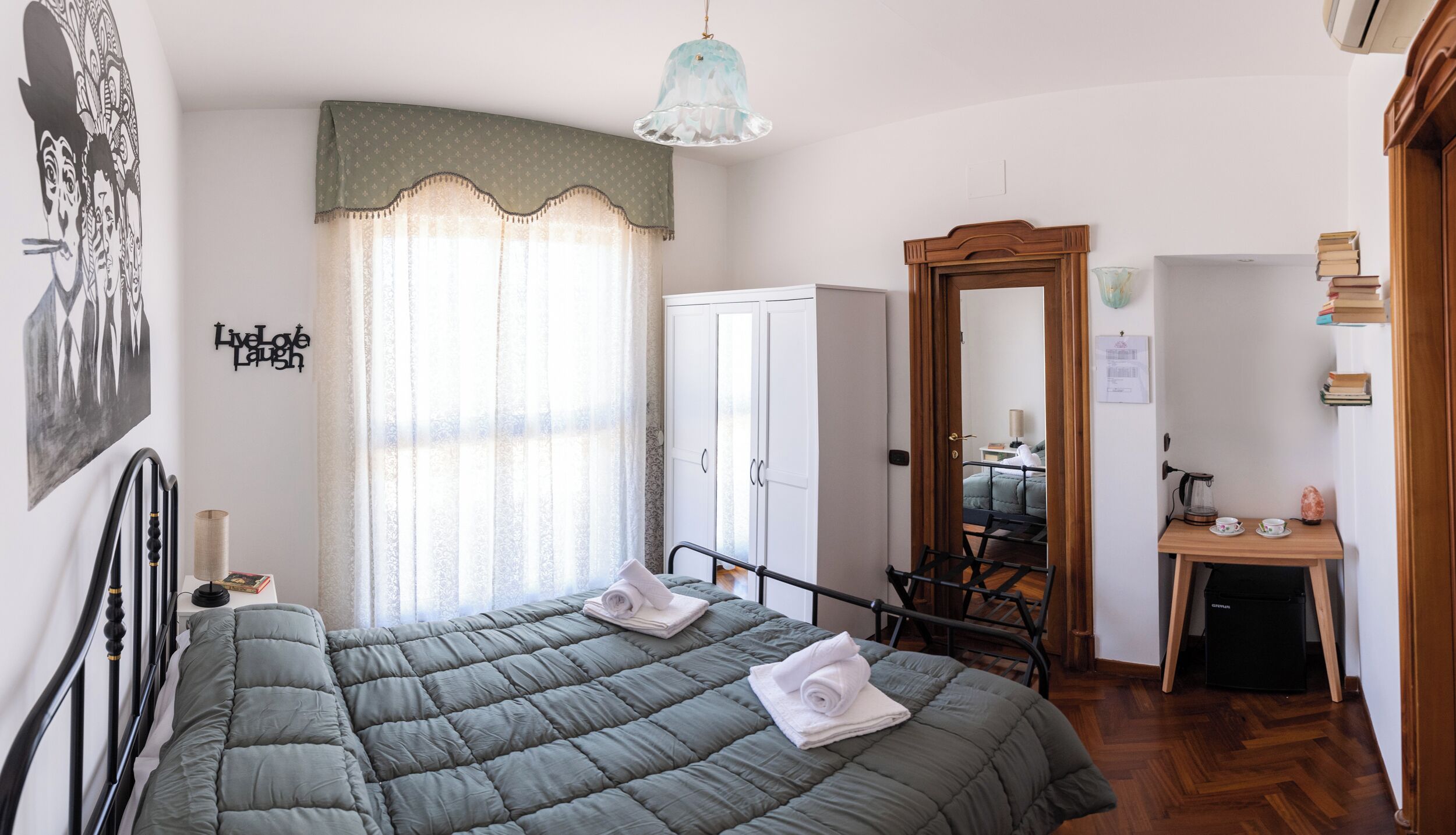 A bedroom with a bed, a wardrobe, a desk, and a mirror.
