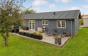A modern house with a grey exterior, a patio with outdoor furniture, and a well-maintained lawn. - 3 bedroom cozy home in Bogense (Bogense)