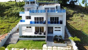 Una casa moderna de varios pisos con un balcón, una escalera y un jardín.