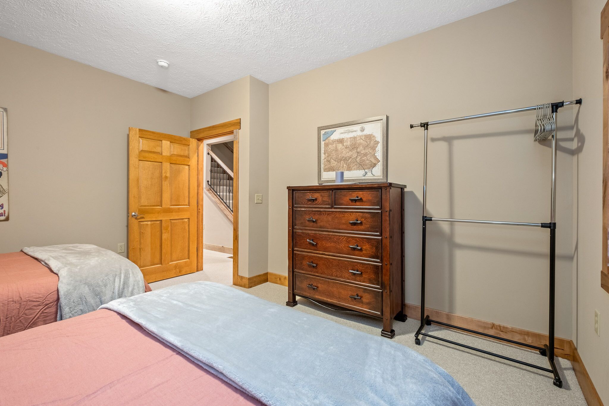 A bedroom with two beds, a wooden dresser, a coat rack, and a framed map on the wall.