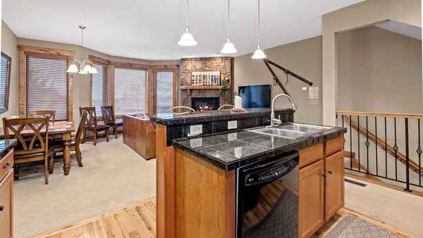 Una cocina moderna con encimeras de granito, armarios de madera y lavavajillas integrado. Cuenta con un comedor con sillas de madera y una mesa, además de una chimenea con revestimiento de piedra.