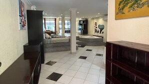 Een ruime woonkamer met tegels, een donker houten bankje, een bank en een televisie.
